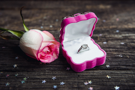 A diamond engagement ring in a jewellery box, shot next to a red rose. On a wooden tableの写真素材