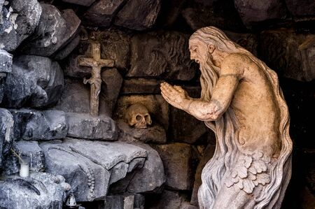 Sculpture of an old man praying. Skull, rocks, crossの写真素材