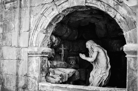 Sculpture of an old man praying. Skull, rocks, cross.. Black and white photoの写真素材