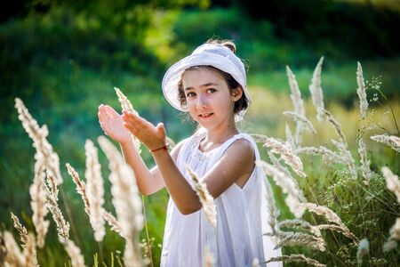 Beautiful toddler girl with long blond hair travels in colorful yellow field through high grassの写真素材