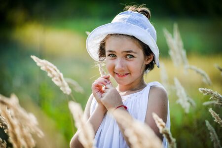 Beautiful toddler girl with long blond hair travels in colorful yellow field through high grassの写真素材