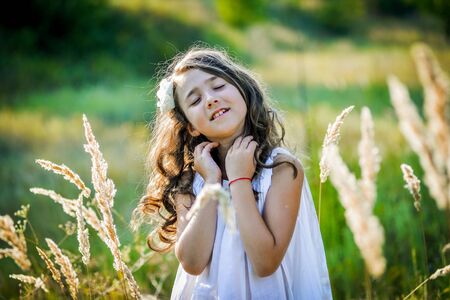 Beautiful toddler girl with long blond hair travels in colorful yellow field through high grassの写真素材