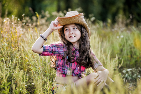 Cute Child having fun outdoors, little girl cowboy playing in wheat field at sunset.の写真素材