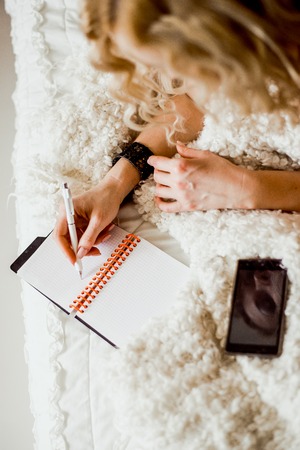 Young woman lying in bed, dreaming with pen.  Girl blonde with wavy hair