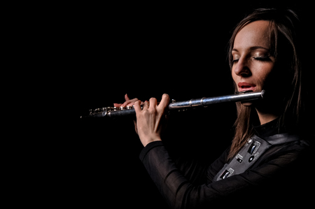 Young elegant woman girl flutist flautist performer playing flute musical instrument on black.の写真素材