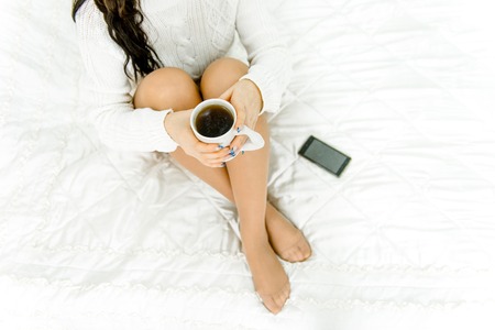 legs girl on the bed with a cup of coffee, mobile phone lying nextの写真素材