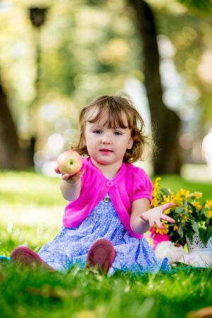 Little girl sitting in the park and eating appleの写真素材