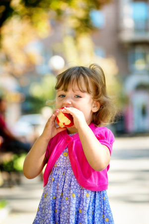 Little girl sitting in the park and eating appleの写真素材