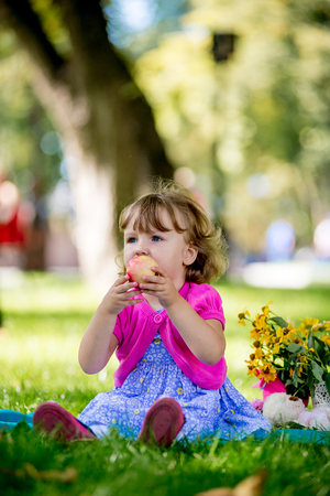 Little girl sitting in the park and eating appleの写真素材
