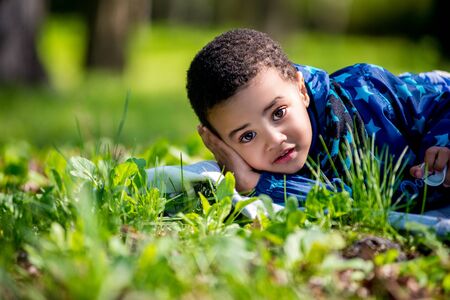 cute happy little boy lying in green grass on spring. black boy
