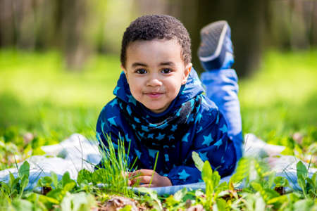 cute happy little boy lying in green grass on spring. black boyの写真素材