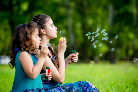 Little girls blow bubbles sitting on the grass. Two sistersの写真素材