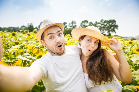 young happy couple man and woman are in a field of sunflowers, make selfie pics, grimace and funの写真素材