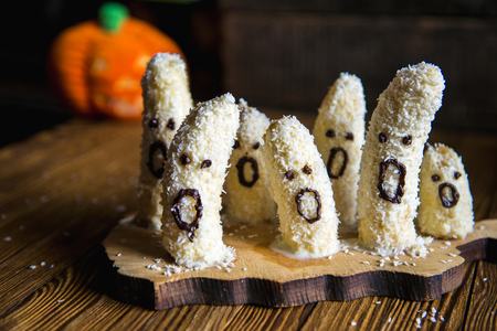 Homemade halloween scary banana ghosts monsters with chocolate faces. funny dessert recipe for party decoration fruits on vintage wooden table backgroundの写真素材