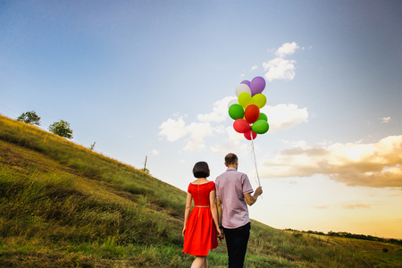 happy couple of man and woman in love, with multi-colored balloons at sunsetの写真素材