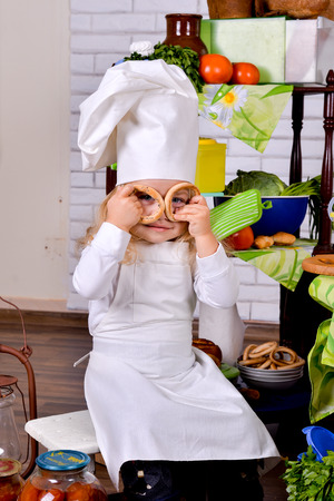 Little girl in a cook clothes with bagels in the hands of. little girl in clothes cooks in the kitchenの写真素材