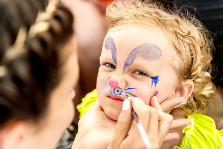 woman painting face of kid outdoors. baby face painting