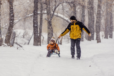Father and son with a sledge outdoor in the snow, snowingの写真素材