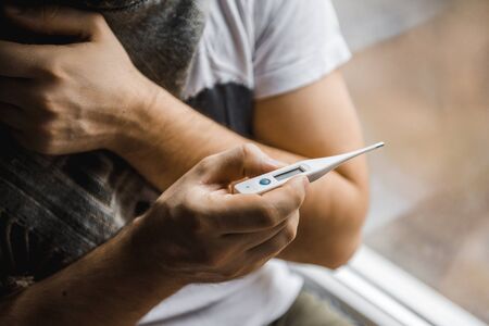 Man feeling bad lying in the bed and looking the thermometer , main focus on the thermometerの写真素材