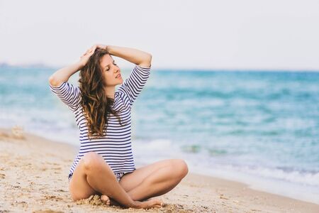 Young beautiful woman during tropical beach vacation. Meditating girl enjoy summer vacation alone on beach in lotus yoga pose.の写真素材