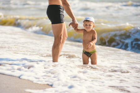 father and son go swim at beach. A child afraid to go into the waterの写真素材
