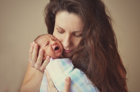 portrait of a newborn baby boy in his mother's shoulder. A newborn baby cries in his mother's arms