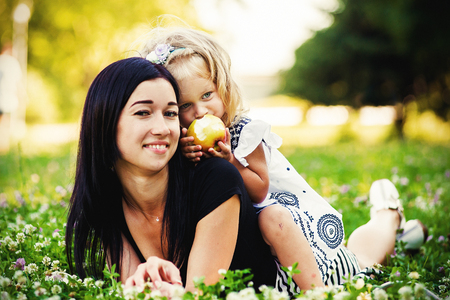 mother and daughter eating an apple in nature. Mother and her child enjoy the early spring, eating apple, happy.の写真素材