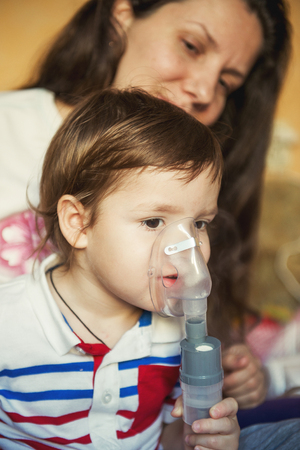 Young woman with son doing inhalation with a nebulizer at homeの写真素材