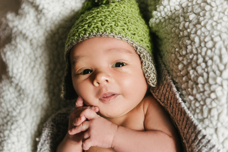 A newborn baby in a hat lies in a crib. The child falls asleep in the cradle