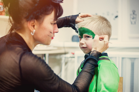 woman painting face of kid outdoors