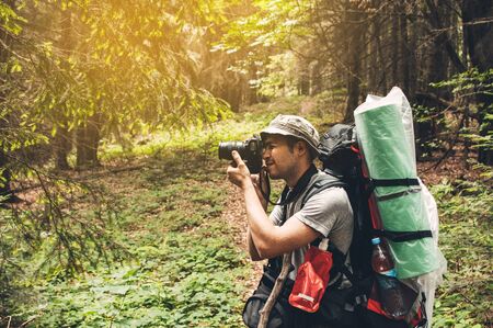 Photographer in the forest. Guys in nature photography forest environment, enjoying the beautiful spring day. Man photographer taking photo of nature. Horizontal shape, side view, copy space.の写真素材
