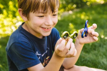 Boy playing with two fidget spinner stress relieving toys outdoorの写真素材