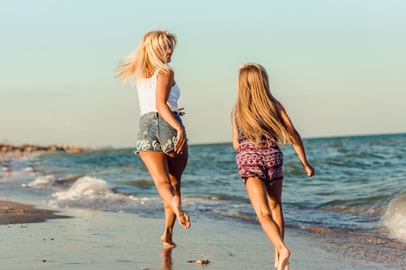 Mother and her little daughter running at tropical beachの写真素材