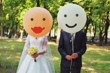 Newlyweds with orange and white balloons. Funny photo with newlyweds. young couple have covered the faces with big orange and white balloons.の写真素材