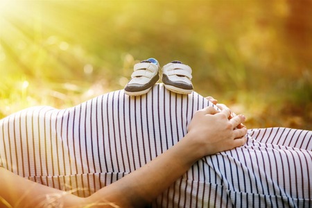 blue baby shoes balancing on pregnant stomach. Booties sneakers on the belly of a pregnant womanの写真素材