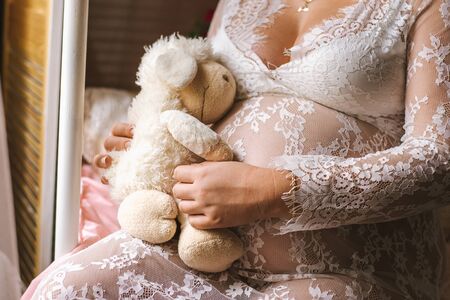 Close-up pregnant woman's belly with soft toy sheep. Pregnancy, parenthood, preparation and expectation concept.の写真素材