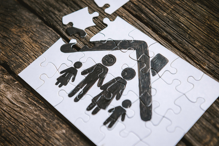 Family concept, puzzle. Father, mother, son and daughter under the roof of a house painted on a puzzleの写真素材