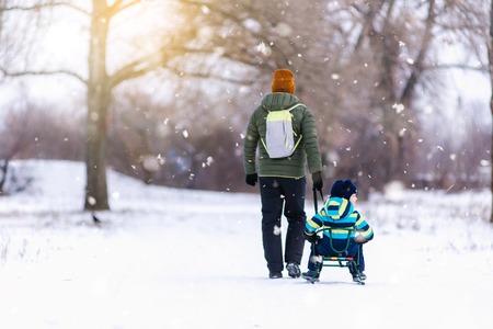 Father and son with a sledge outdoor in the snow, snowing