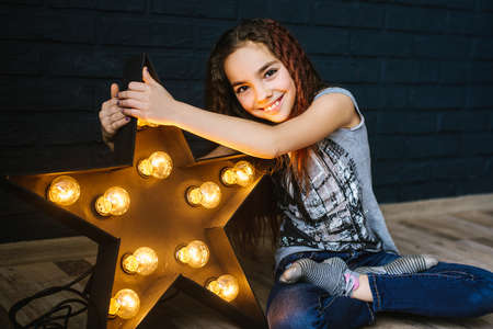 A little girl with long dark hair with a star glowing in her hands. The concept of fame, luck, celebrityの写真素材
