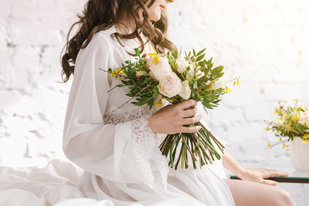 Close-up of a bride peignoir with bouquet of flowers in hands. Morning of the bride. Bride's fees. Underwear. Bed.の写真素材