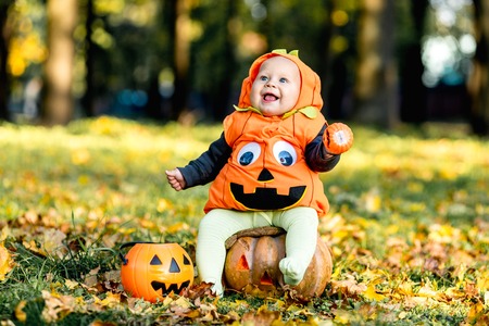 Child in pumpkin suit on background of autumn leavesの写真素材