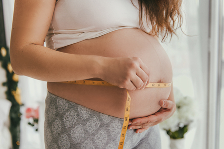 Pregnant woman in underwear measures belly using a measuring tapeの写真素材