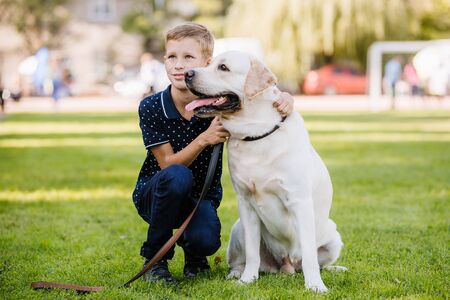 Portrait of cute adorable little Caucasian baby boy sitting with dog in park outside. Smiling child...