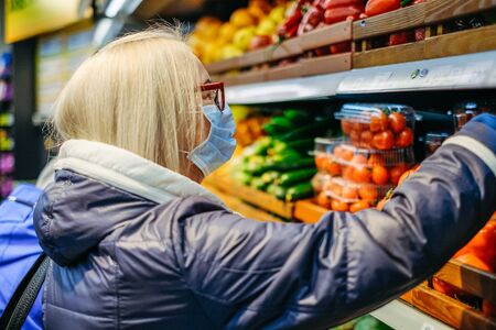 Old woman in medical masks is shopping in the supermarket looking for the foodの写真素材