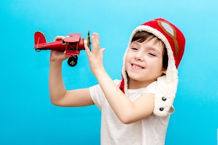 An impressive boy in a pilots cap raised his hands up holding a retro toy airplane, isolated on a...