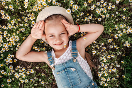 Pretty girl lying in daisy field and smiling to camera, unity with nature, childhoodの写真素材