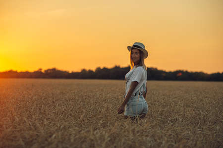 Young girl with outspread hands standing standing in the wheat field at sunset