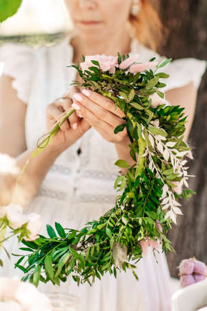 Workshop florist, making bouquets and flower arrangements. Girl makes wreath at head. Process of weaving a wreath with herbs and flowers. Lesson of florists close-up. Copy spaceの写真素材
