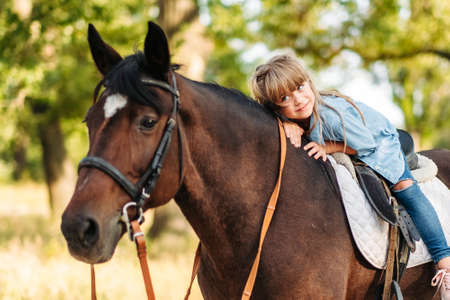 Cute little girl with long hair riding a horse outdoors. Pet therapyの写真素材