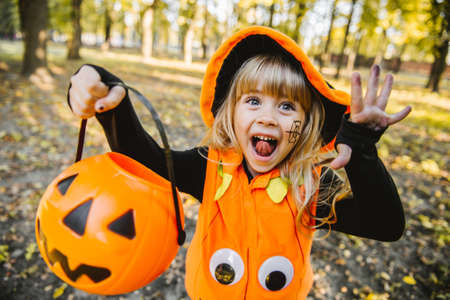 Happy Halloween! Cute little witch with a basket in the parkの写真素材
